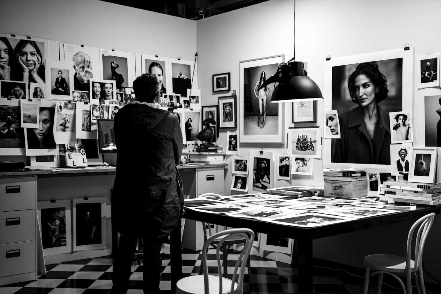 Artista che guarda delle stampe in uno studio in bianco e nero.