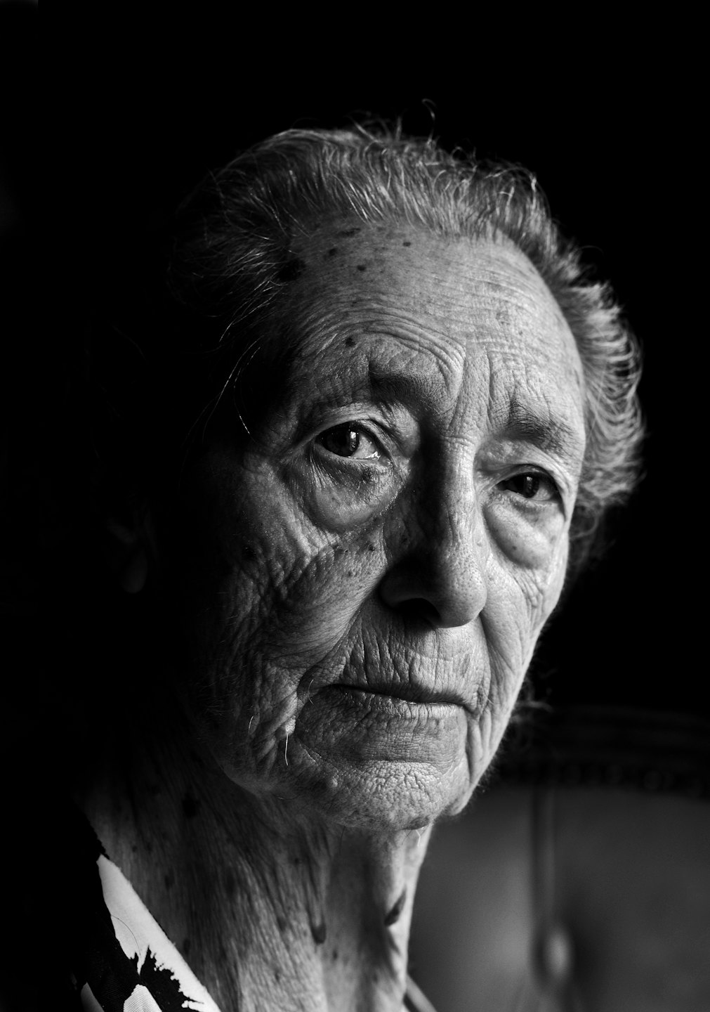 Donna anziana con rughe profonde guarda pensierosa verso la macchina fotografica.
