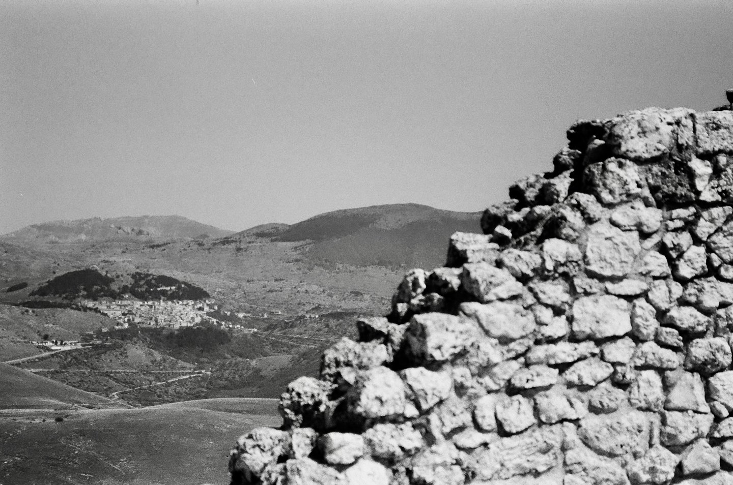 Muro di pietra davanti a un villaggio tra dolci colline.
